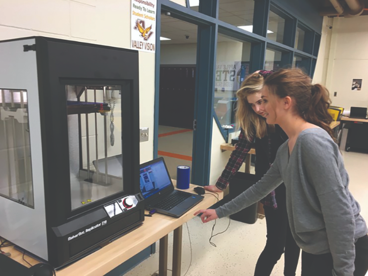 Two Apple Valley High School students watch the part they designed print.