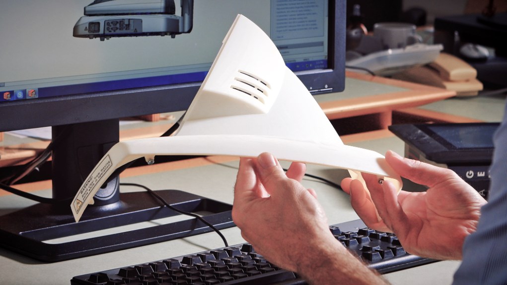 a white 3d printed part being examined next to a computer monitor