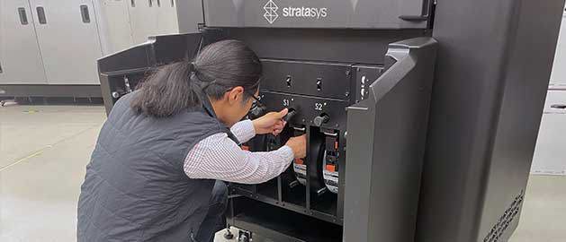 Stratasys Direct employee loading an FDM material spool into an industrial 3D printer.