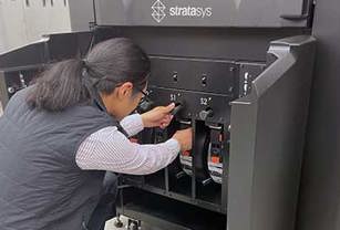 Stratasys Direct employee loading an FDM material spool into an industrial 3D printer.