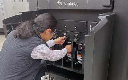 Stratasys Direct employee loading an FDM material spool into an industrial 3D printer.