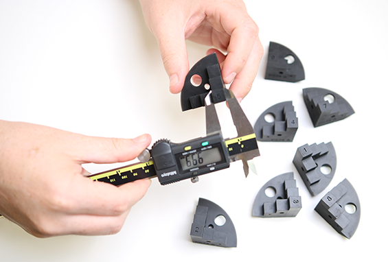 Close-up of hands using a digital caliper to measure precision 3D-printed black plastic components for quality inspection.