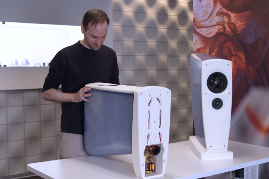 Designer assembling a custom 3D-printed speaker enclosure prototype next to a completed high-end speaker model.